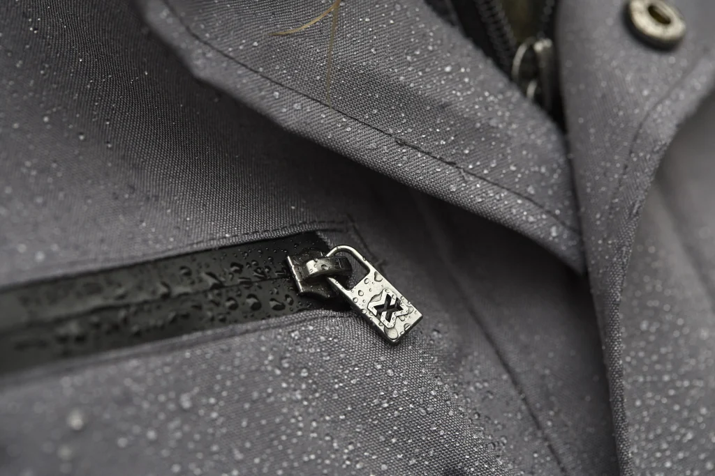 Zoom sur le tissu noir d'une veste Stretch X humide, remplie de gouttes d'eau