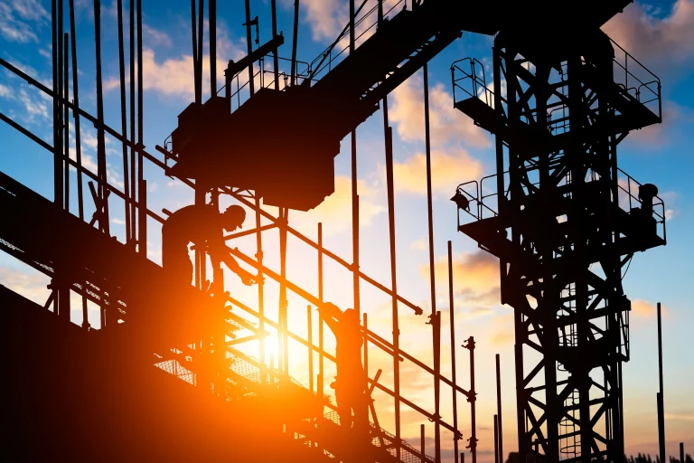 Un lever de soleil sur un chantier. Un ouvrier travail sur des échafaudages, à coté d'une grue en contrejour